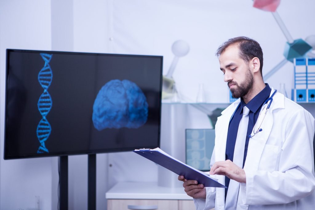 Confident young doctor with clipboard his hands standing by monitor with brain graph handsome doctor