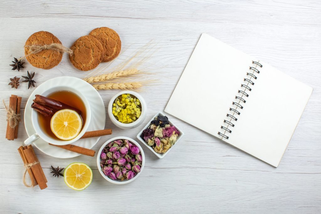 Top view black tea with cinnamon lime lemon various herbals cookies open notebook white background