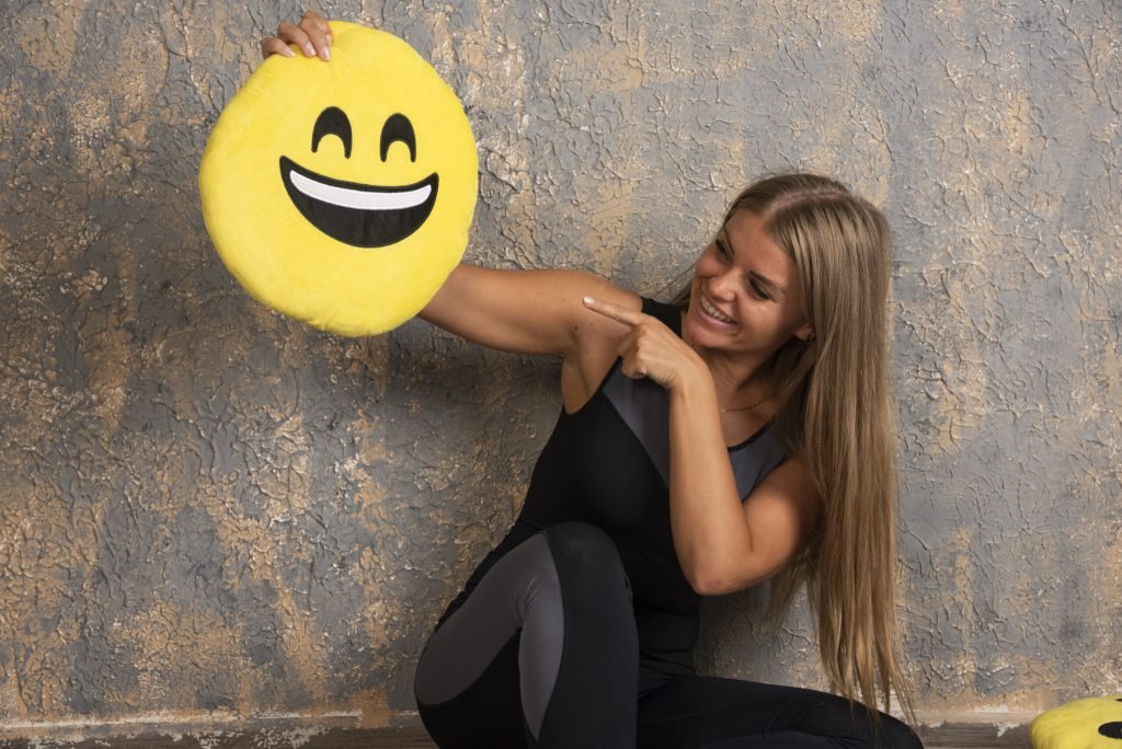 Young sportive girl sport outfits holding smiling emoji pillow pointing it