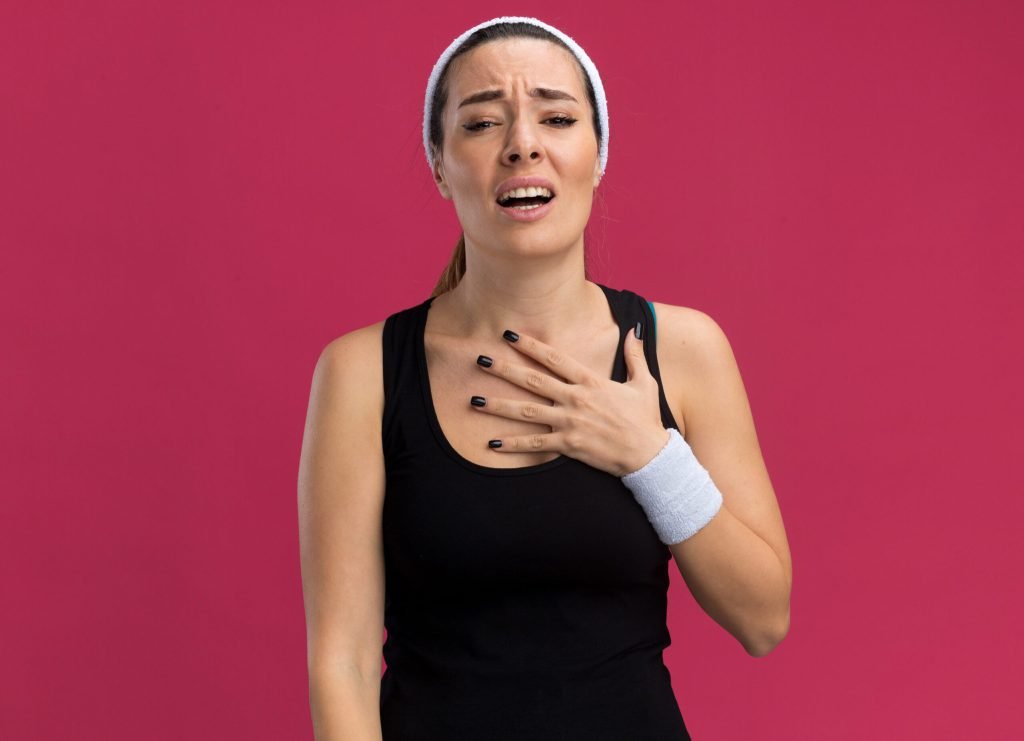 Aching young pretty sporty woman wearing headband wristbands putting hand chest