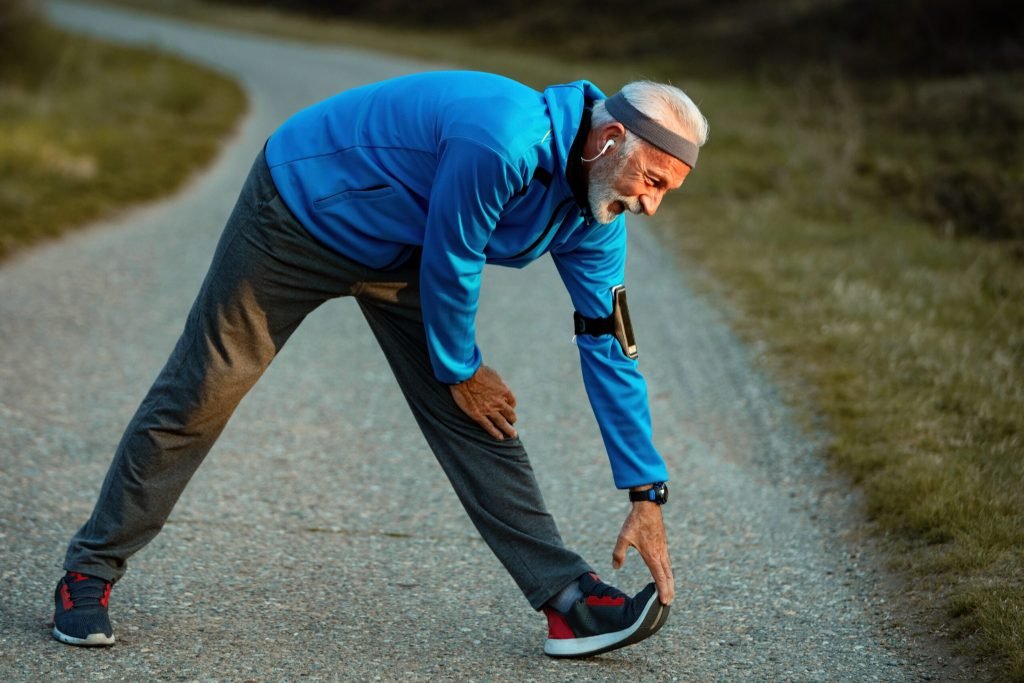 Mature sportsman warming up before run stretching road nature