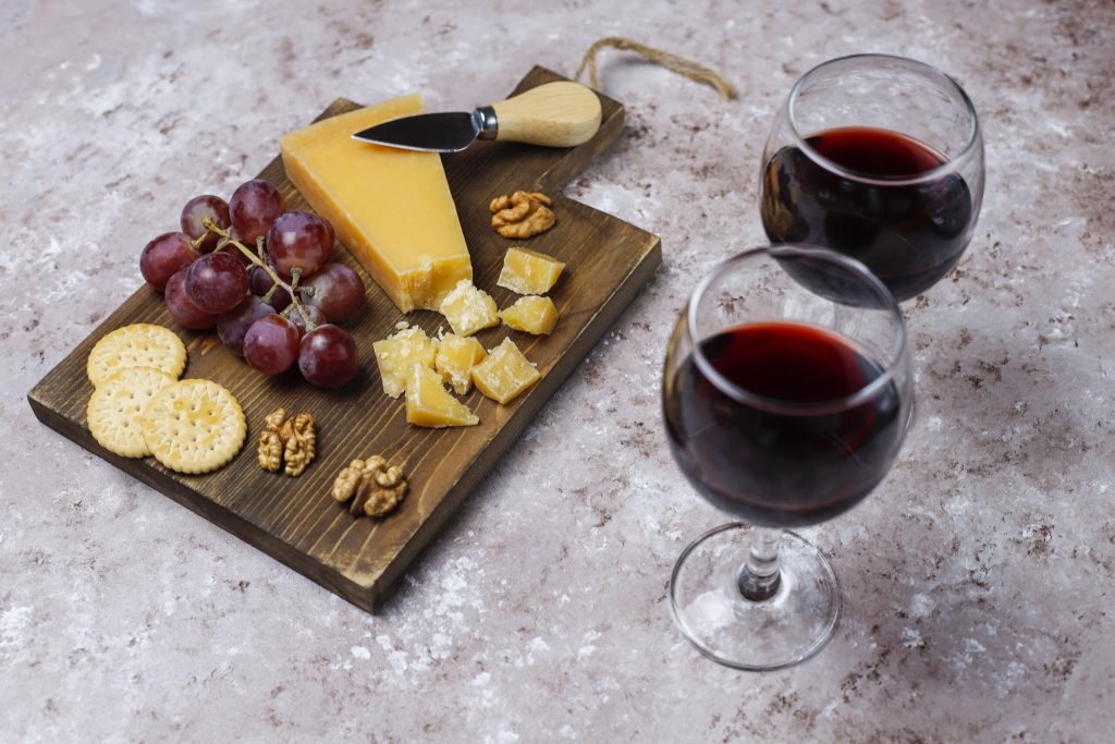 Cheese board with hard cheese cheese knife red wine glass grape brown concrete surface
