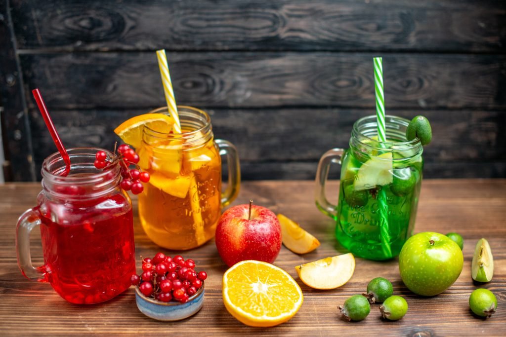 Front view fresh fruity juice orange feijoa cranberry drinks inside cans brown desk drink photo cocktail color fruits