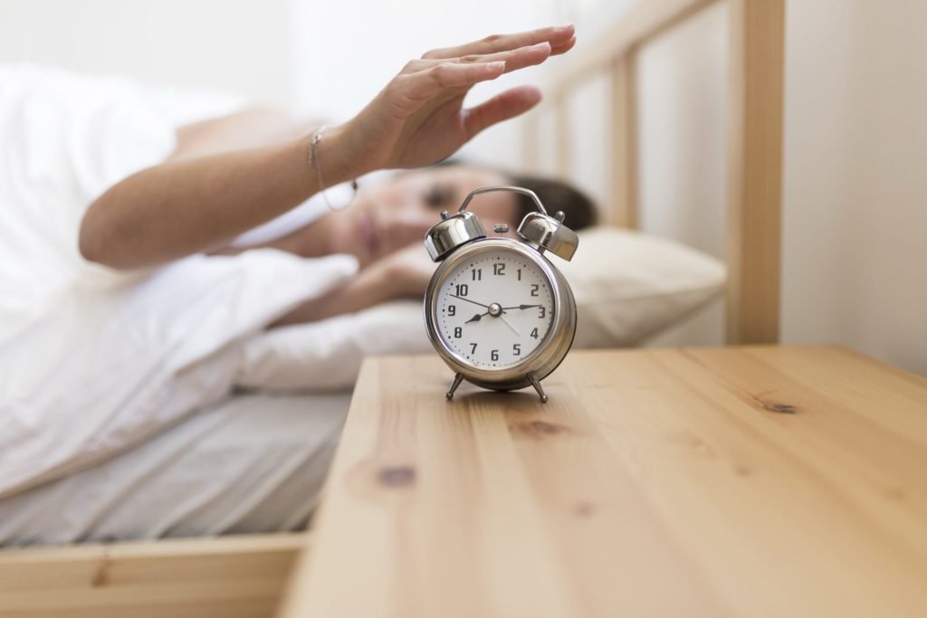 Woman turning off alarm clock while lying bed