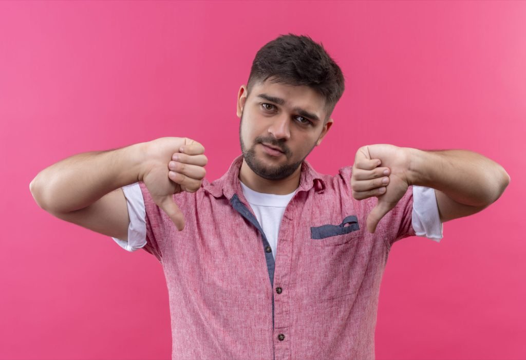 Young handsome guy wearing pink polo shirt doing unhappy thumbs down standing pink wall