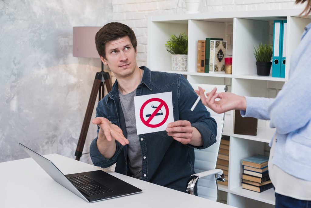 Young man sitting office showing no smoking sign woman holding cigarette