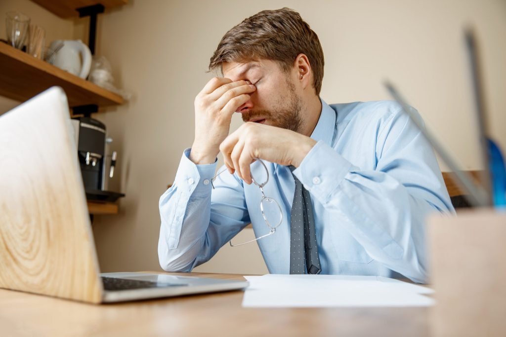 Feeling sick tired frustrated sad unhappy sick young man massaging his head while sitting his working place office
