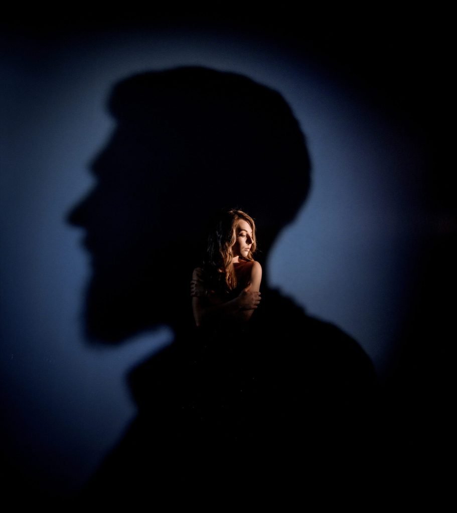 Tender caucasian blonde girl with closed eyes is standing man s head shadow blue wall