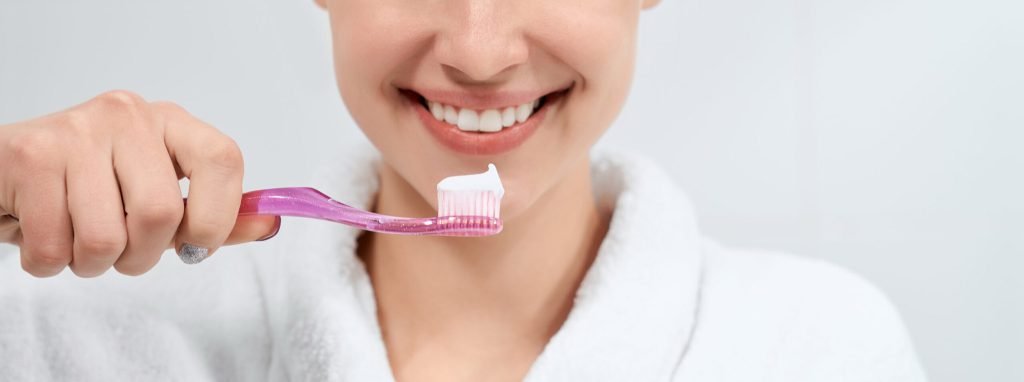 Woman white robe holding toothbrush with paste