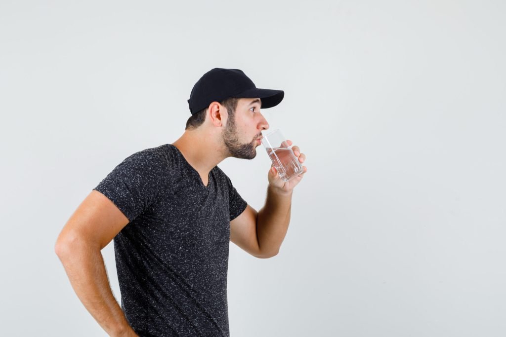 Young male drinking water t shirt cap looking thirsty