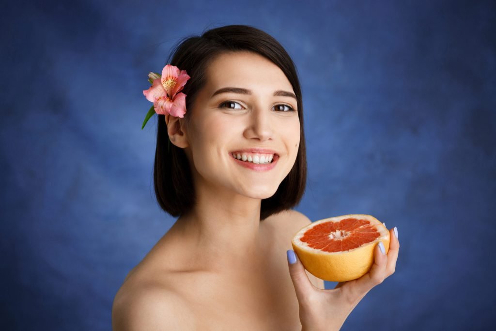 Close up portrait tender young woman holding cut orange blue wall