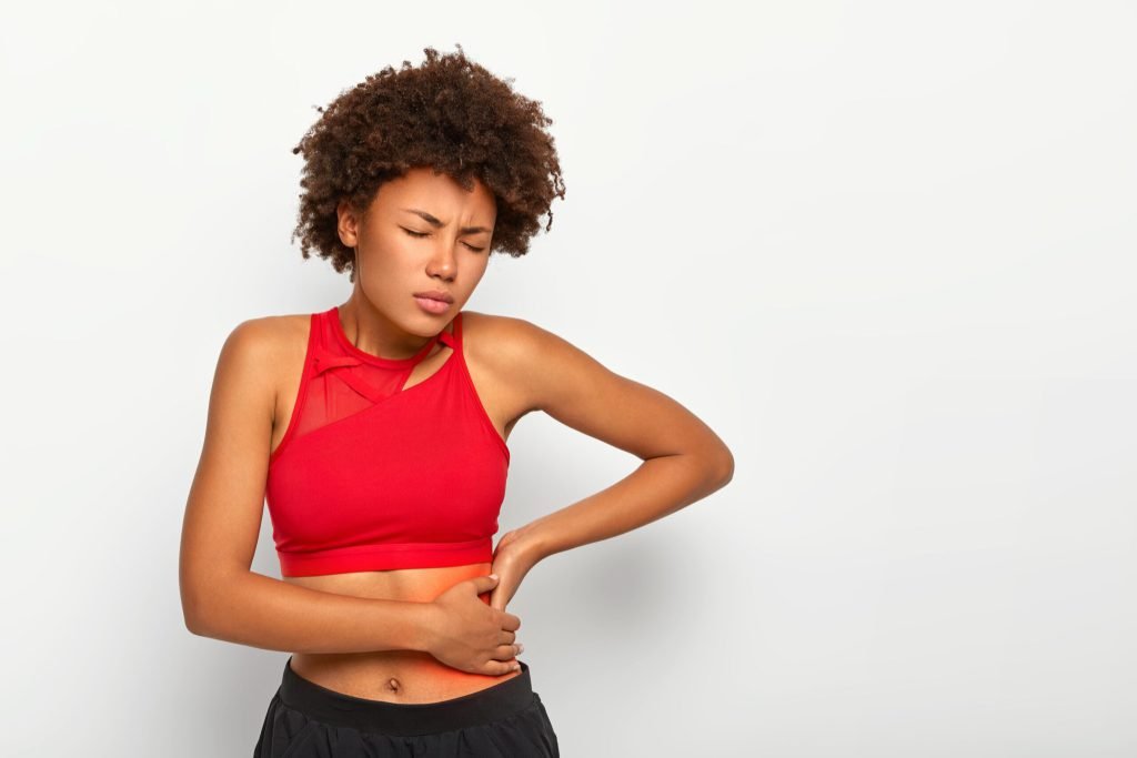 Dissatisfied woman holds aching hip has kidney inflammation touches location pain near ribs marked with red dot wears spor...