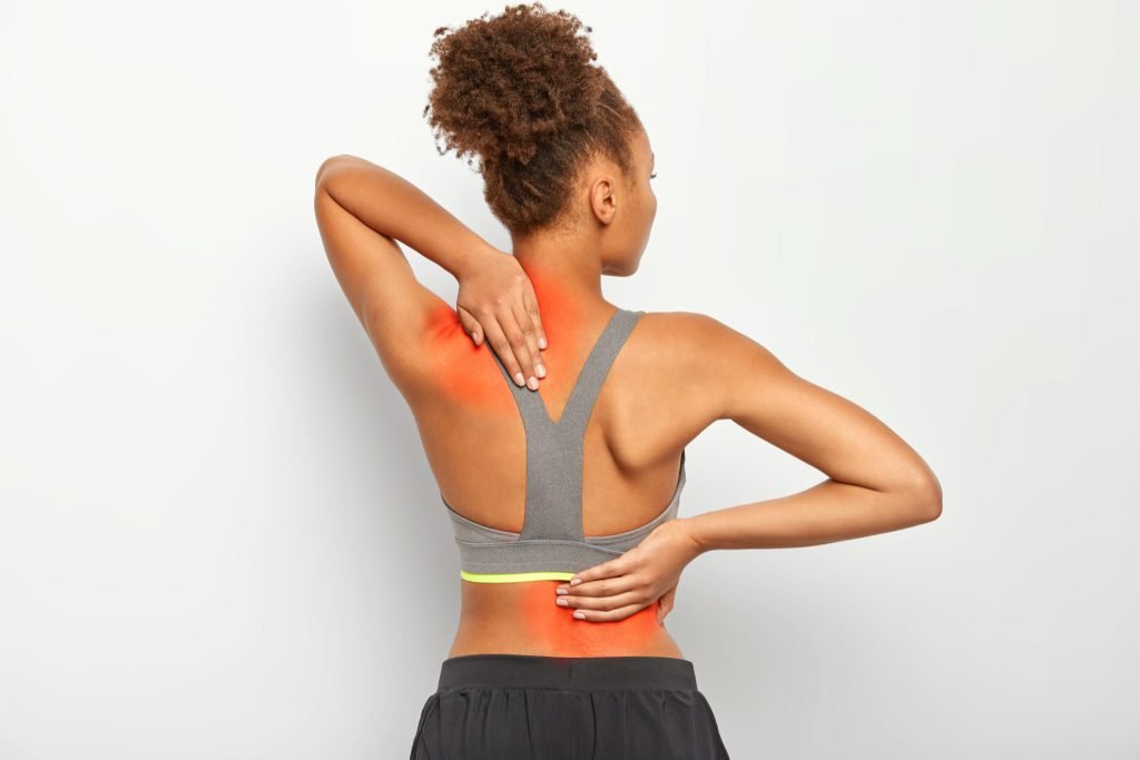 Faceless curly woman suffers from spine pain wears sport bra shows location inflammation isolated white background