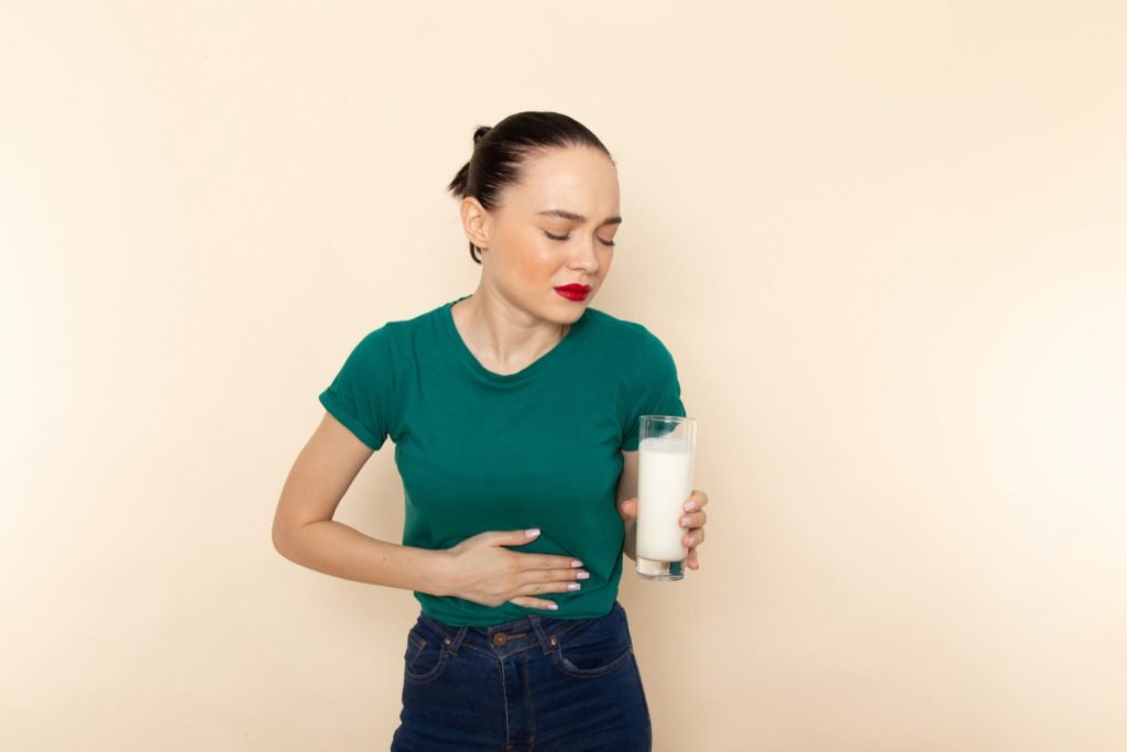 Front view young female dark green shirt blue jeans holding milk having stomachache beige