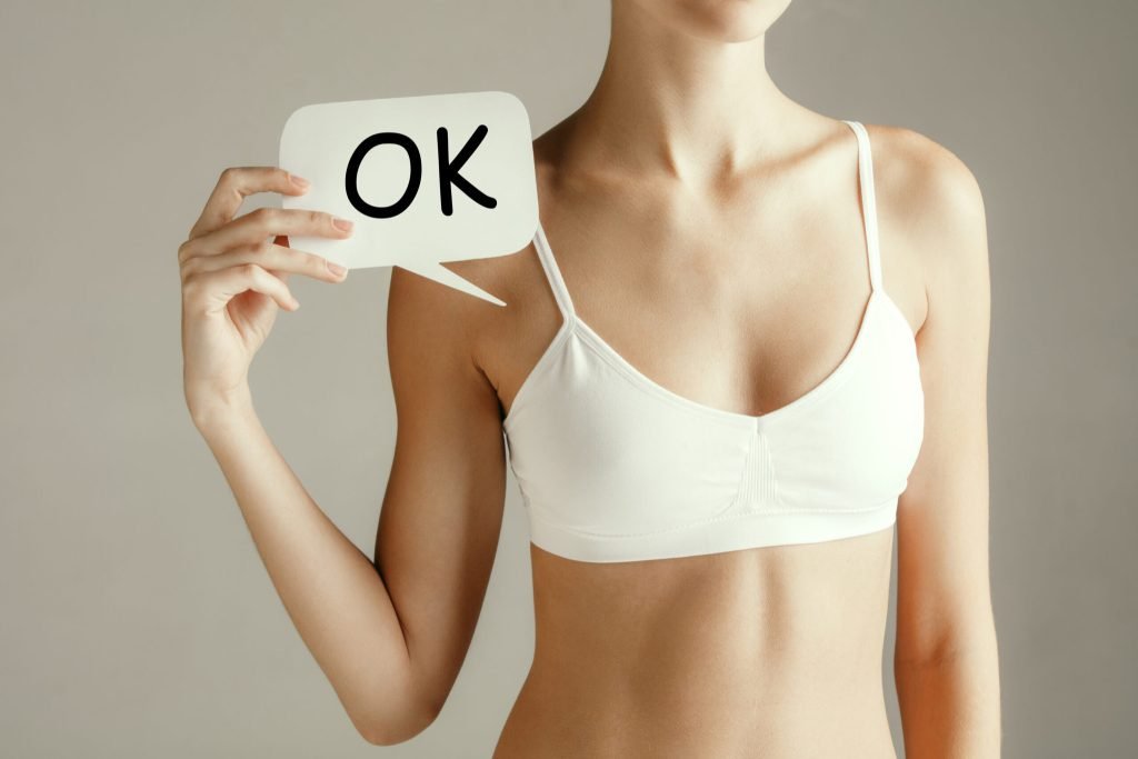 Woman health female model holding card near breast young adult girl with paper positive symbol ok isolated gray background