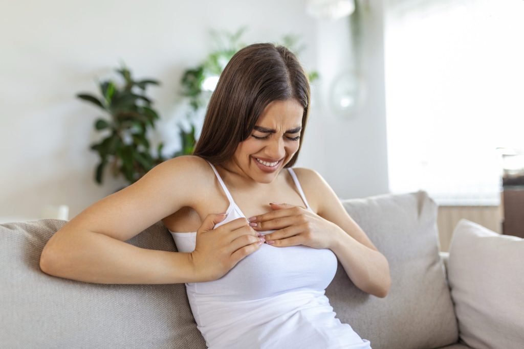Woman sitting with strong chest pain hands touching her chest while having trouble home heart attack heart failure symptom
