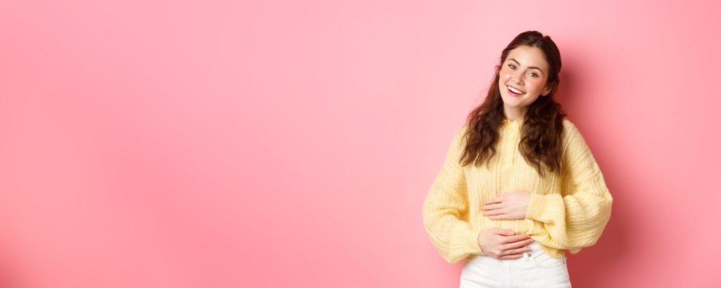 Young smiling woman touching her stomach with relieved happy face feeling good after eating yoghurt