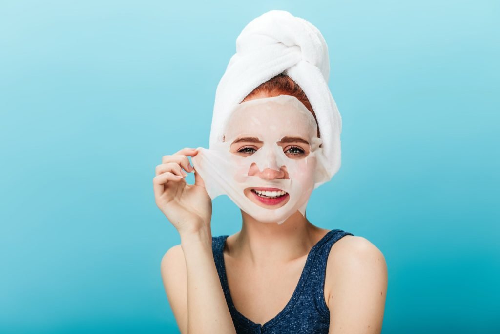 Front view smiling girl taking off face mask studio shot blissful woman with towel head posing blue background