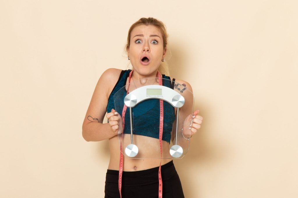 Front view young female sport outfit holding scales white wall fit body sport beauty health exercise