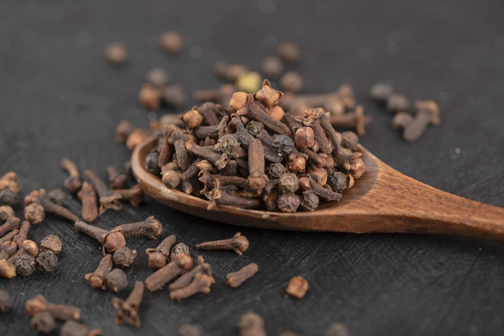 Pile dried natural cloves with wooden spoon black surface