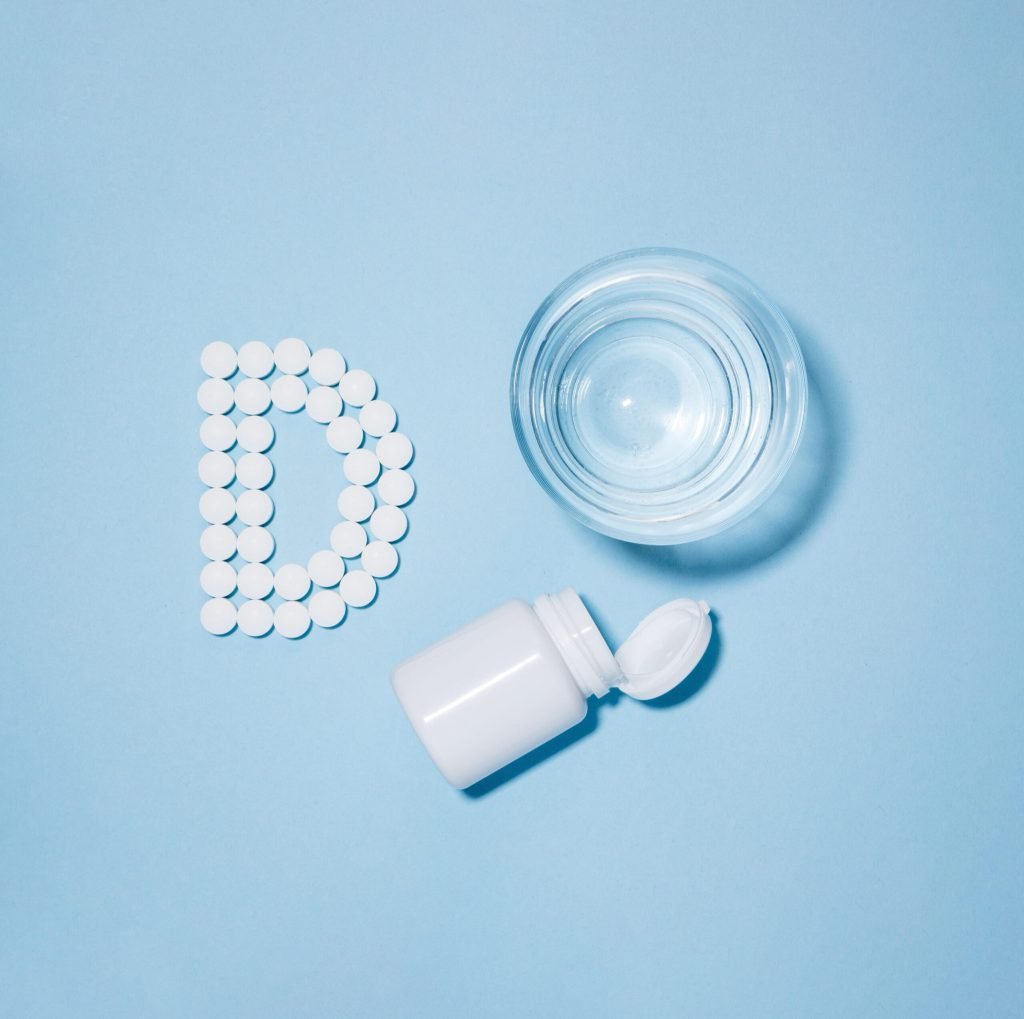 Top view glass water container with pills spelling letter d