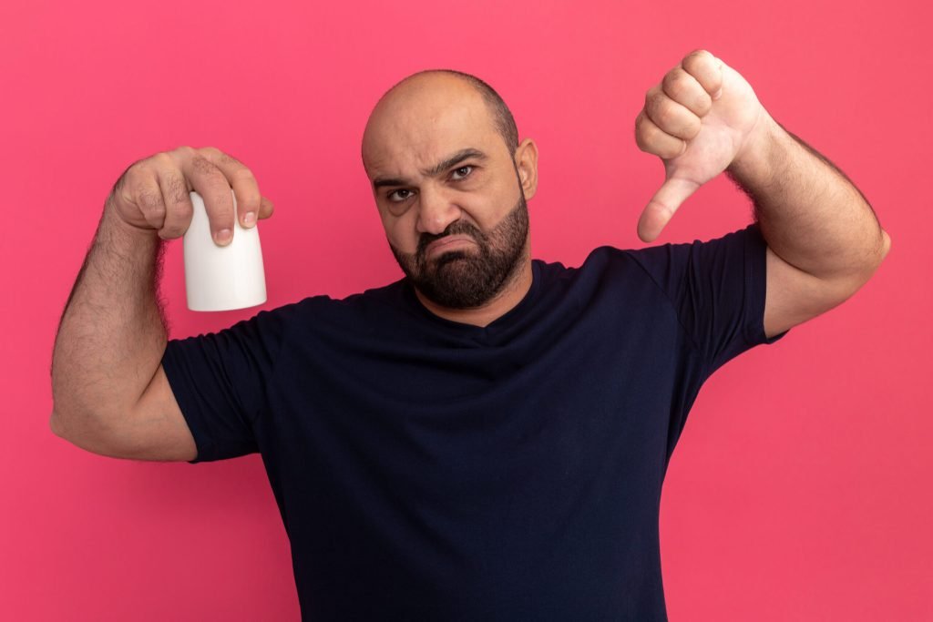 Bearded man navy t shirt holding cup being displeased showing thumbs down standing pink wall