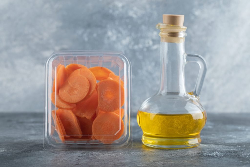 Plastic container full with carrot slices bottle oil grey background
