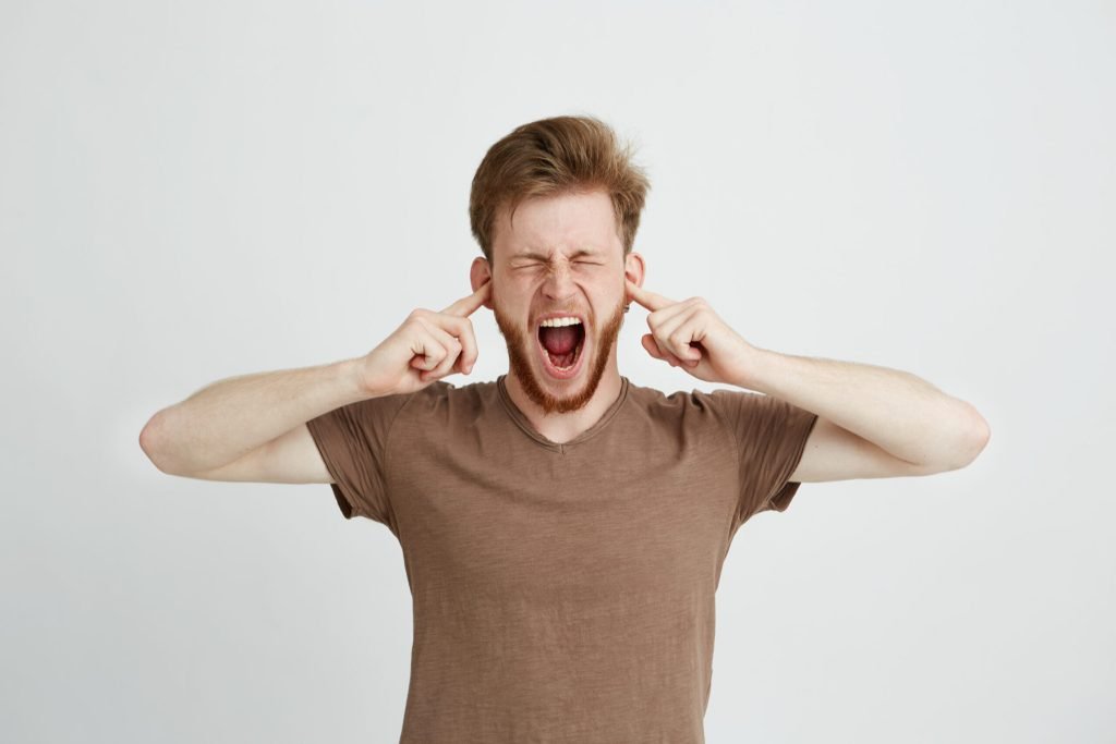 Portrait young emotive angry man closing ears shouting screaming