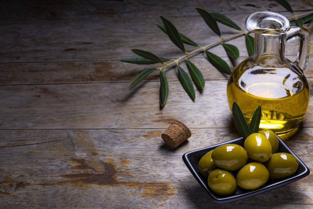 Tasty looking olives extra virgin olive oil olive leafs dark wooden background