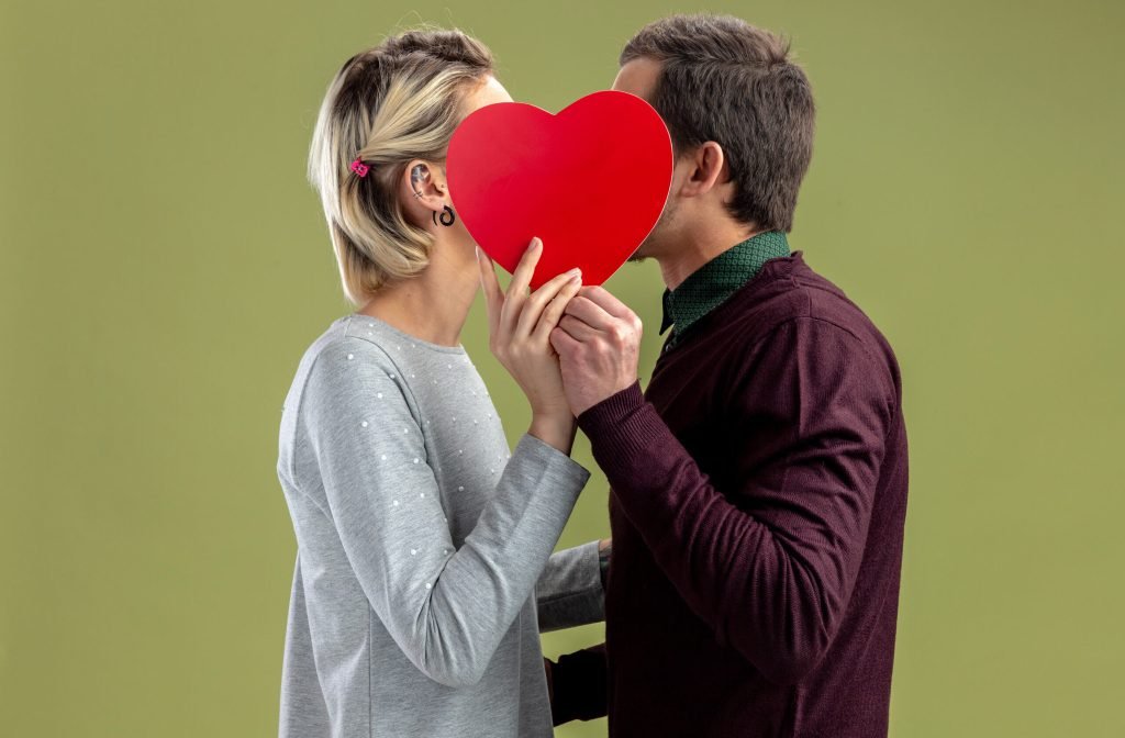 Young couple valentines day covered face with heart shaped box isolated olive green background