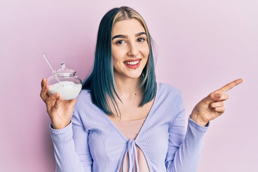 Young modern girl holding bowl with sugar smiling happy pointing with hand finger side