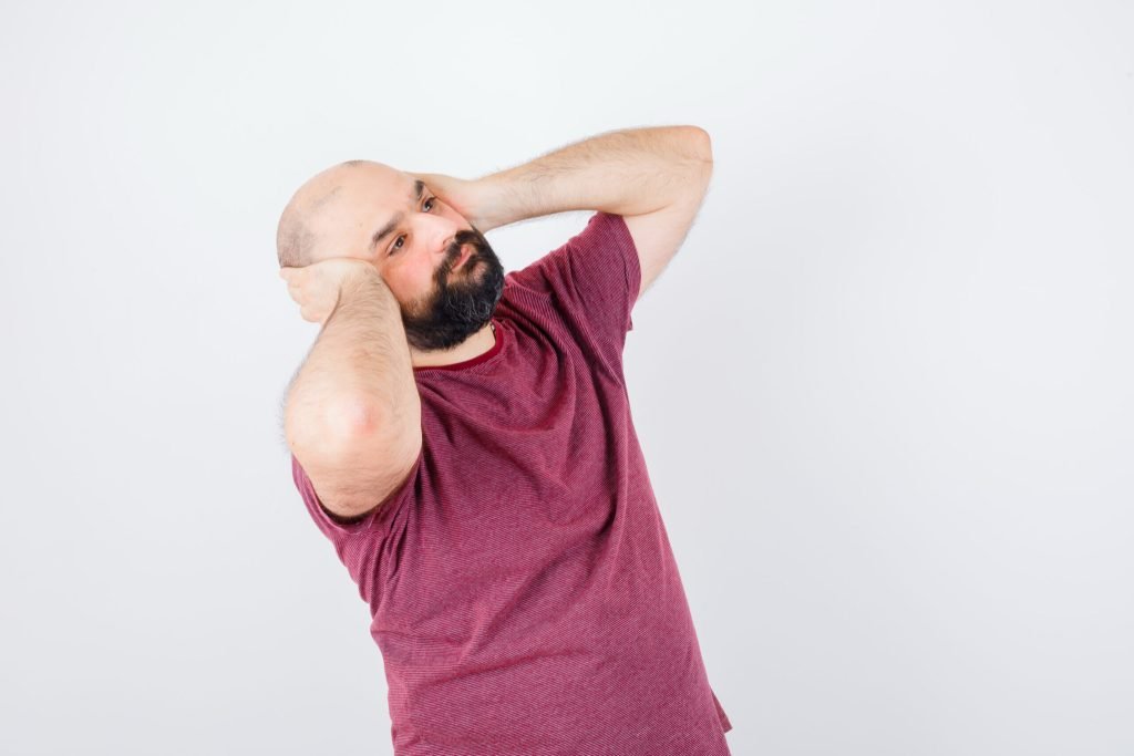 Young male pink t shirt holding hands ears while looking up looking bored