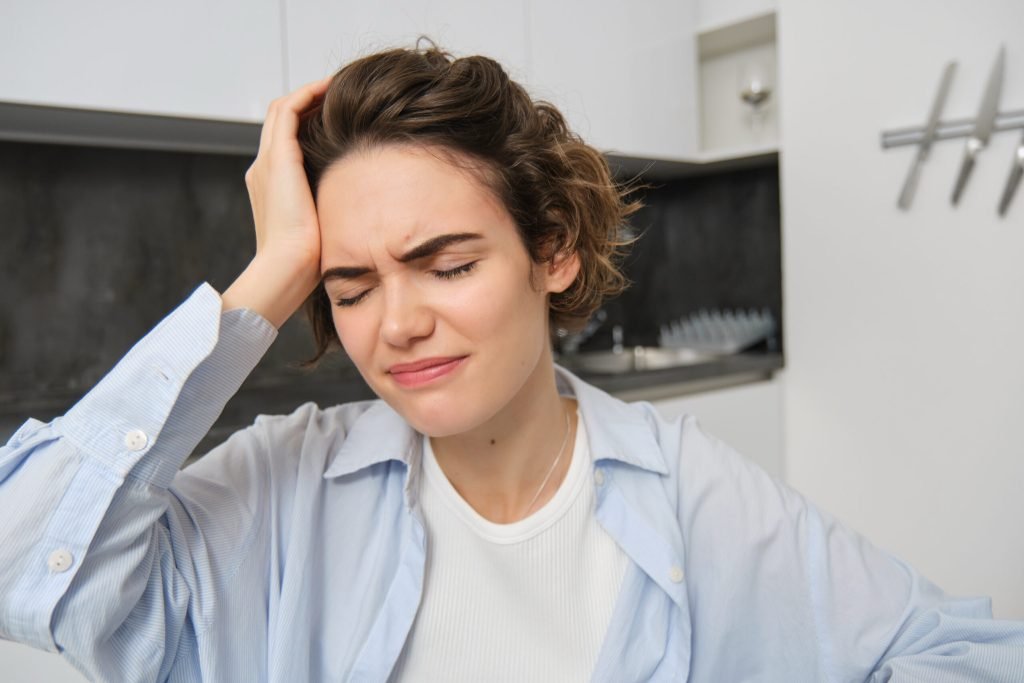 Portrait woman with mgiraine girl grimaces from painful headache touches her head frowns from