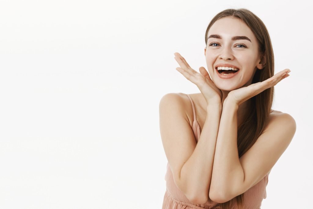 Beautiful healthy charming woman with natural beauty holding palms near jawline smiling broadly pleased with perfect skin ...