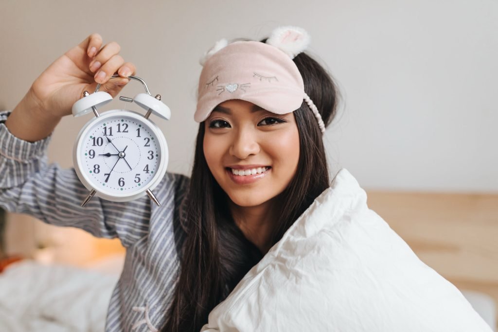 Brown eyed woman high spirits keeps alarm clock smiles looks into front