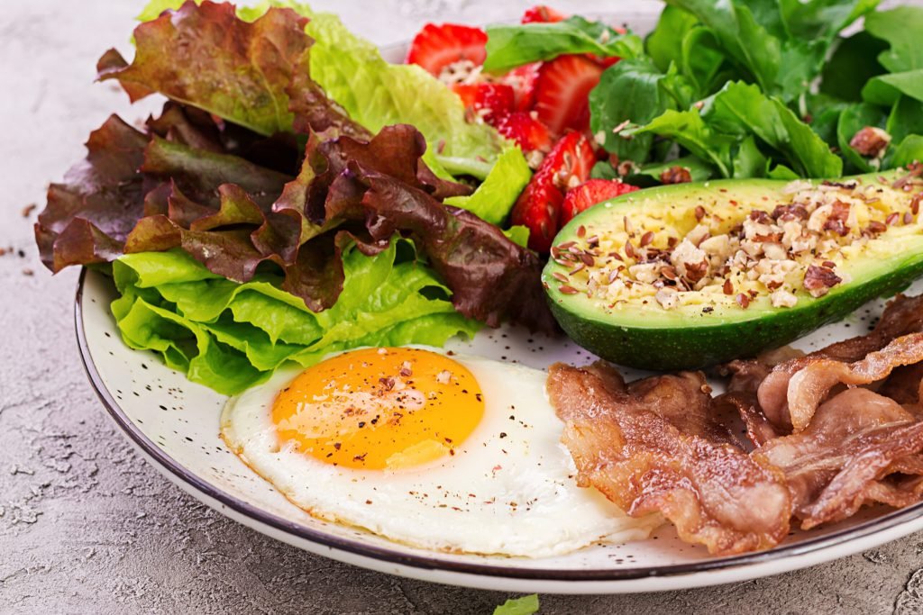 Plate with keto diet food fried egg bacon avocado arugula strawberries keto breakfast