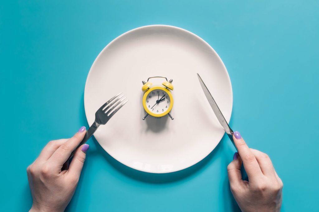 Hands holding knife fork alarm clock plate blue background
